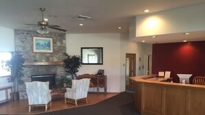 Eine Lobby mit Kamin aus Stein, zwei weißen Sesseln, einem hölzernen Empfangstresen und einem Deckenventilator.