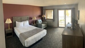 Ein Hotelzimmer mit einem großen Bett, einem Schreibtisch, einem Stuhl und einem fensterbepflanzten Fenster.