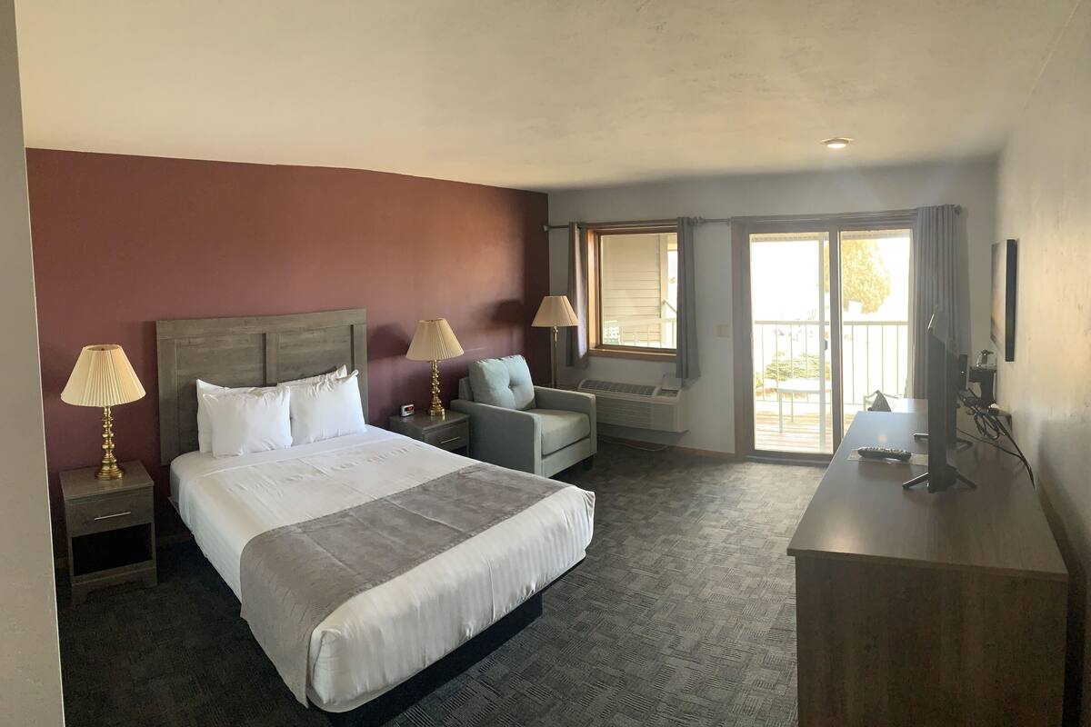 A hotel room with a large bed, a desk, a chair, and a window with curtains.