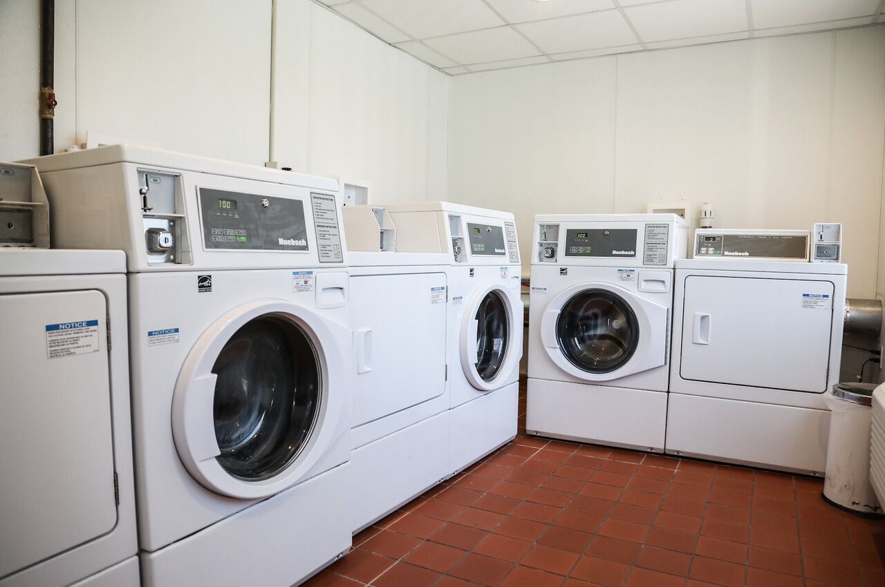 Un cuarto de lavandería con cuatro lavadoras y secadoras blancas, cada una con paneles de control.