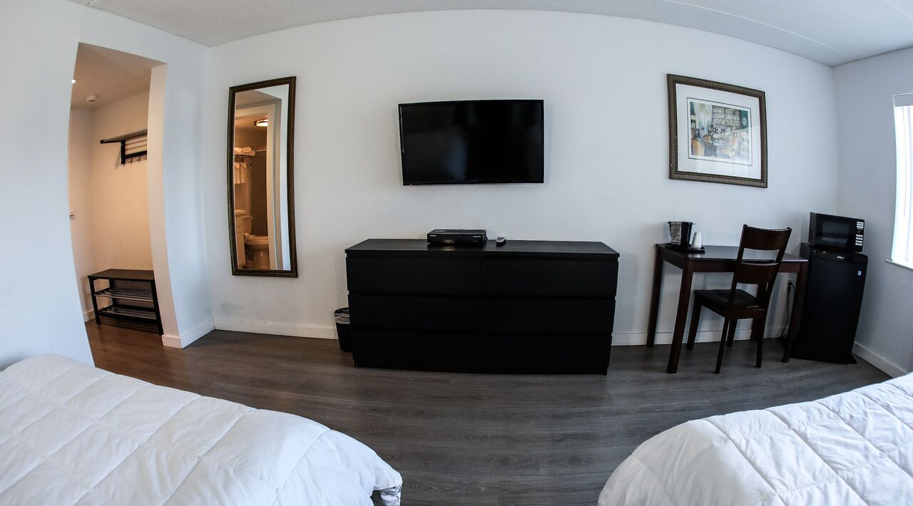 Et hotelværelse med et fladskærms-tv, et skrivebord med stol, en mikrobølgeovn og en kommode.