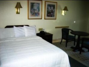 Una camera d'albergo con un letto grande, due quadri appesi alla parete, una scrivania con una sedia e un tavolino.