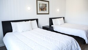 A hotel room with two single beds, a nightstand, and a framed picture on the wall.