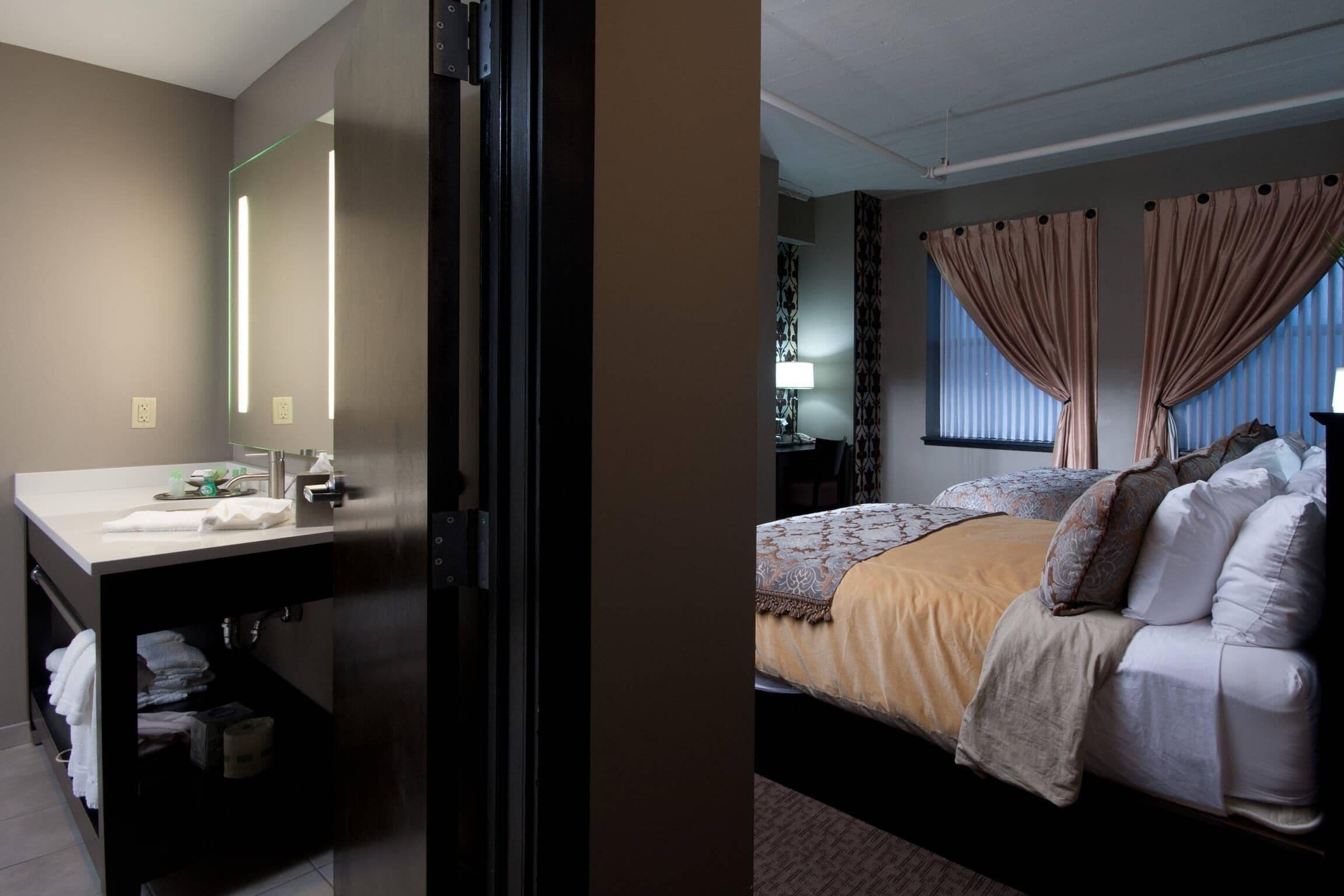 Een moderne hotelkamer met een groot bed, een nachtkastje, een ingebouwd bureau met spiegel en een raam met gordijnen.