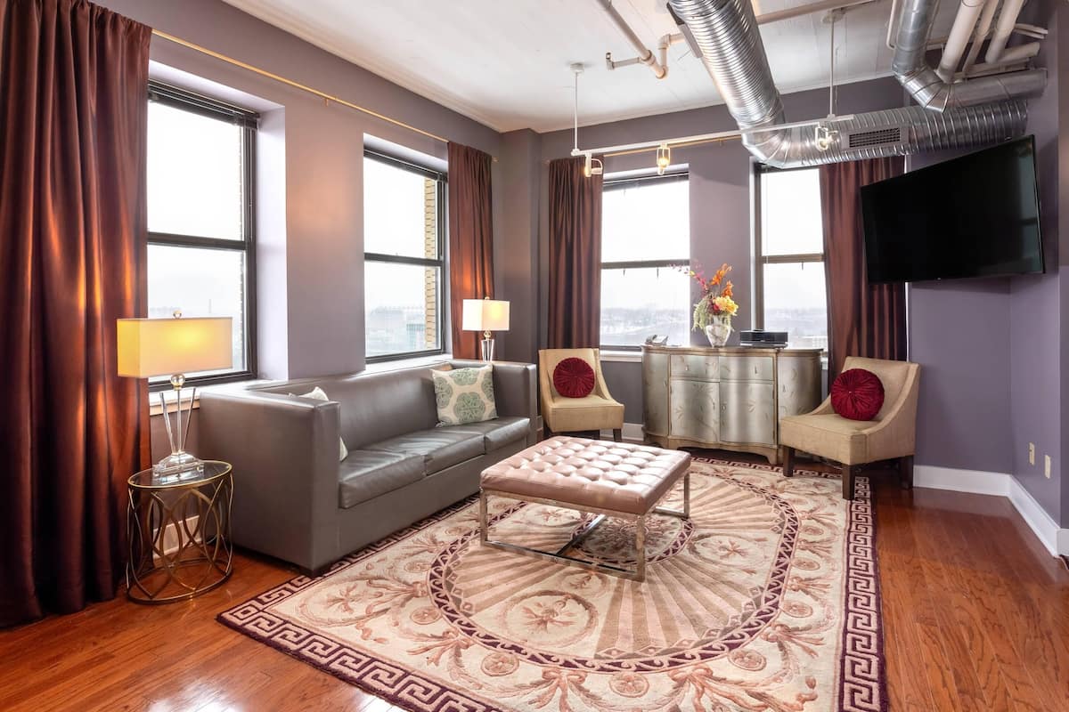 A modern living room with a grey sofa, a round ottoman, and a patterned rug.