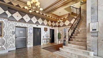 A lobby with a grand staircase, a chandelier, and patterned walls.