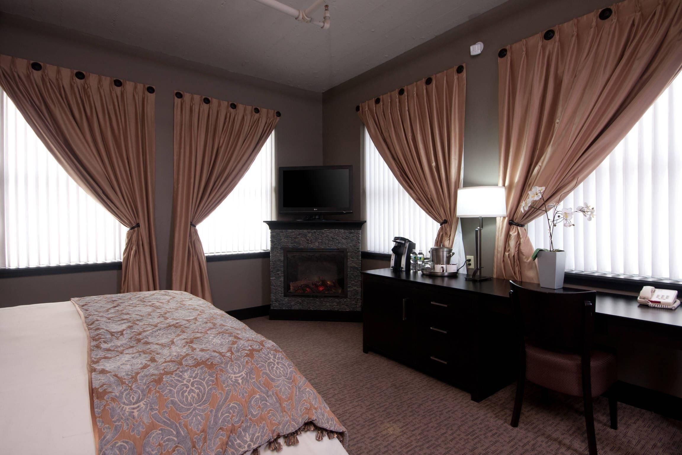 Una habitación de hotel con cama, escritorio, televisor, chimenea y cortinas.