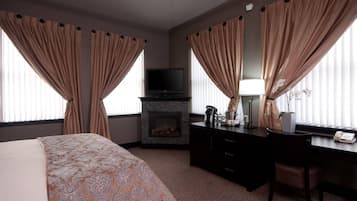 Una habitación de hotel con cama, escritorio, televisor, chimenea y cortinas.