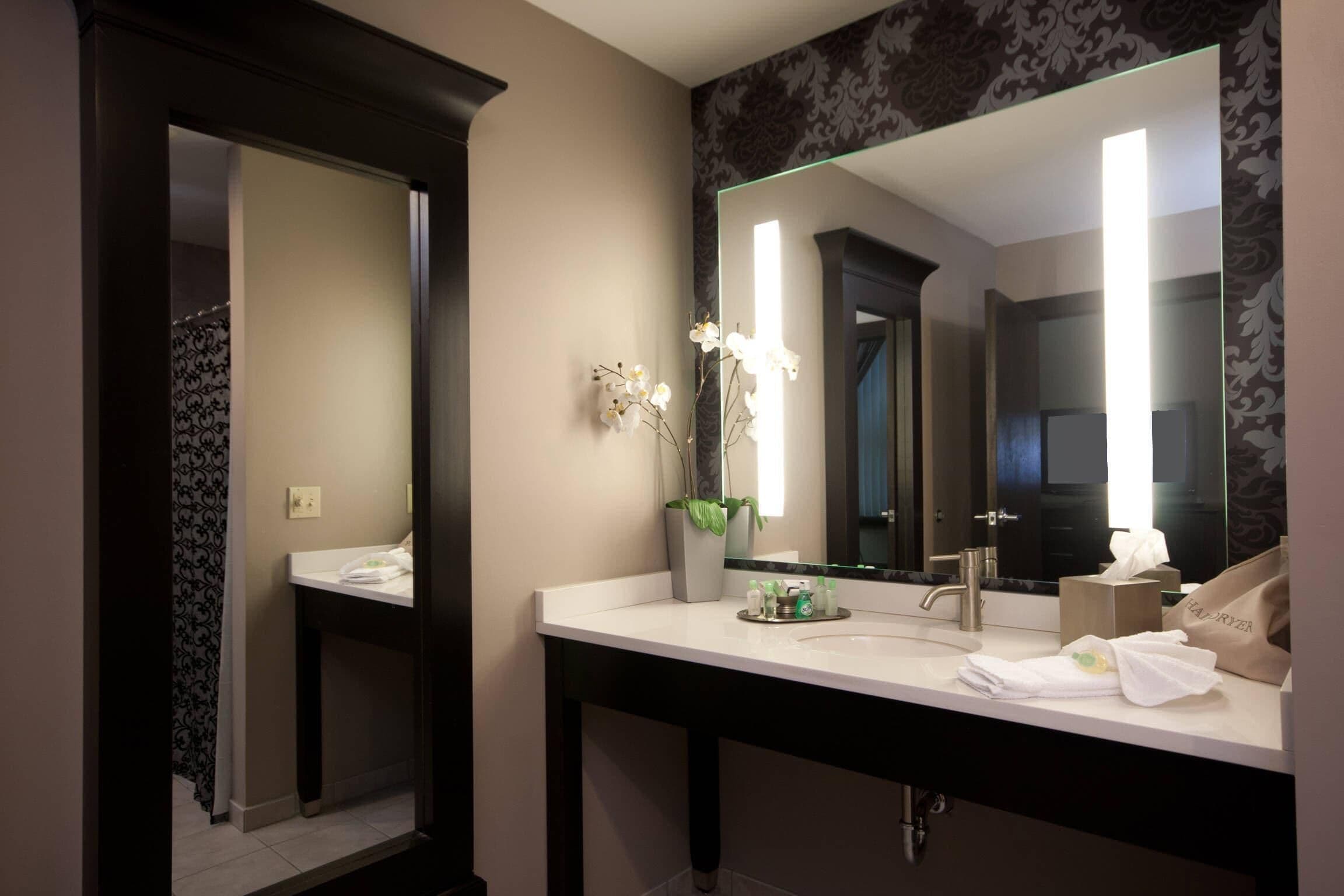 A bathroom with a white sink, dark wooden vanity, a large mirror, and a potted orchid.