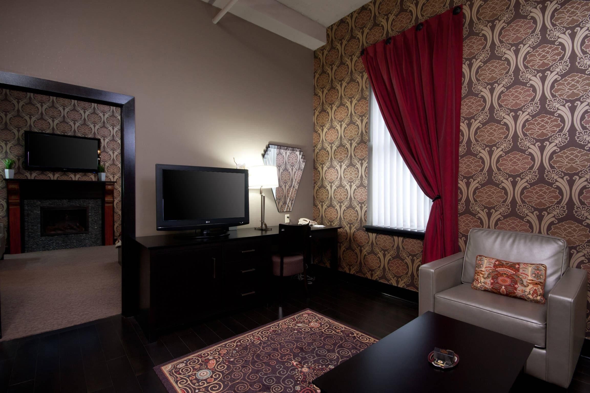 Una sala de estar con televisor de pantalla plana, chimenea, escritorio, una silla y papel tapiz estampado.