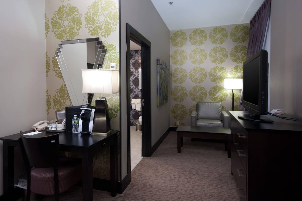 A hotel room with a desk, chair, television, and a mirror.