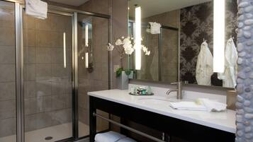 A modern bathroom with a glass shower enclosure, a white sink with a mirror, and a decorative orchid plant.