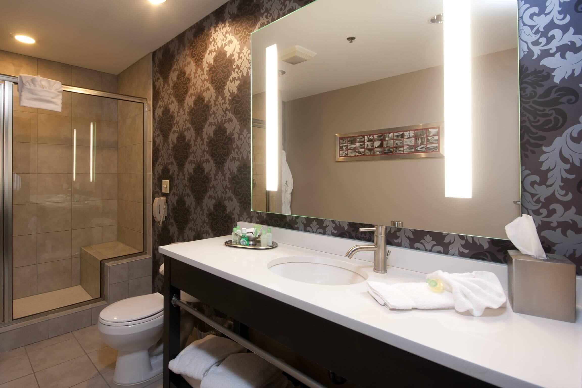 A modern bathroom with a glass-enclosed shower, a white sink, and a large mirror.