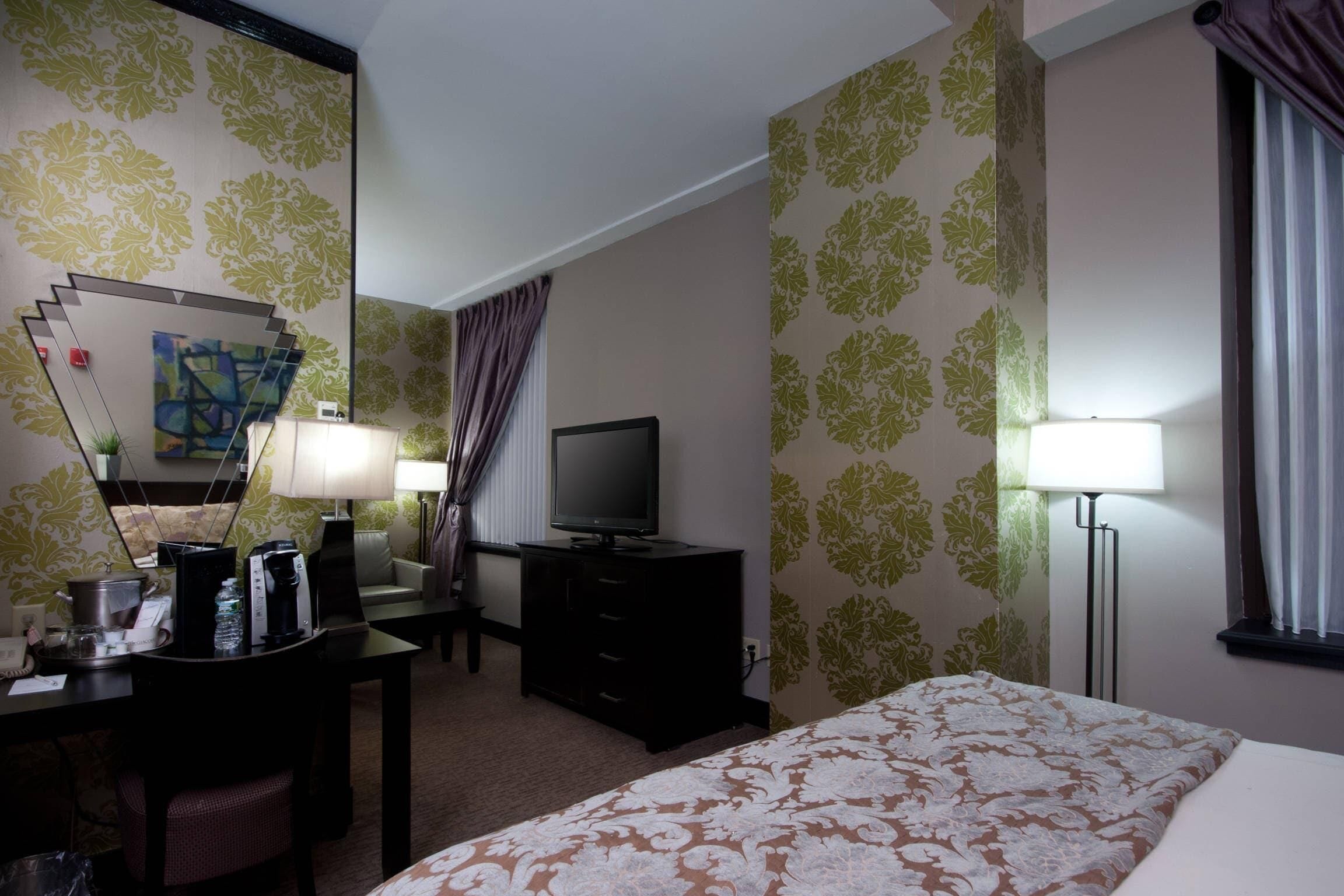 A hotel room with a bed, a desk with a lamp, a television, and a coffee maker.