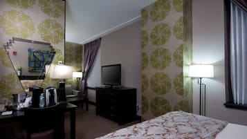 A hotel room with a bed, a desk with a lamp, a television, and a coffee maker.