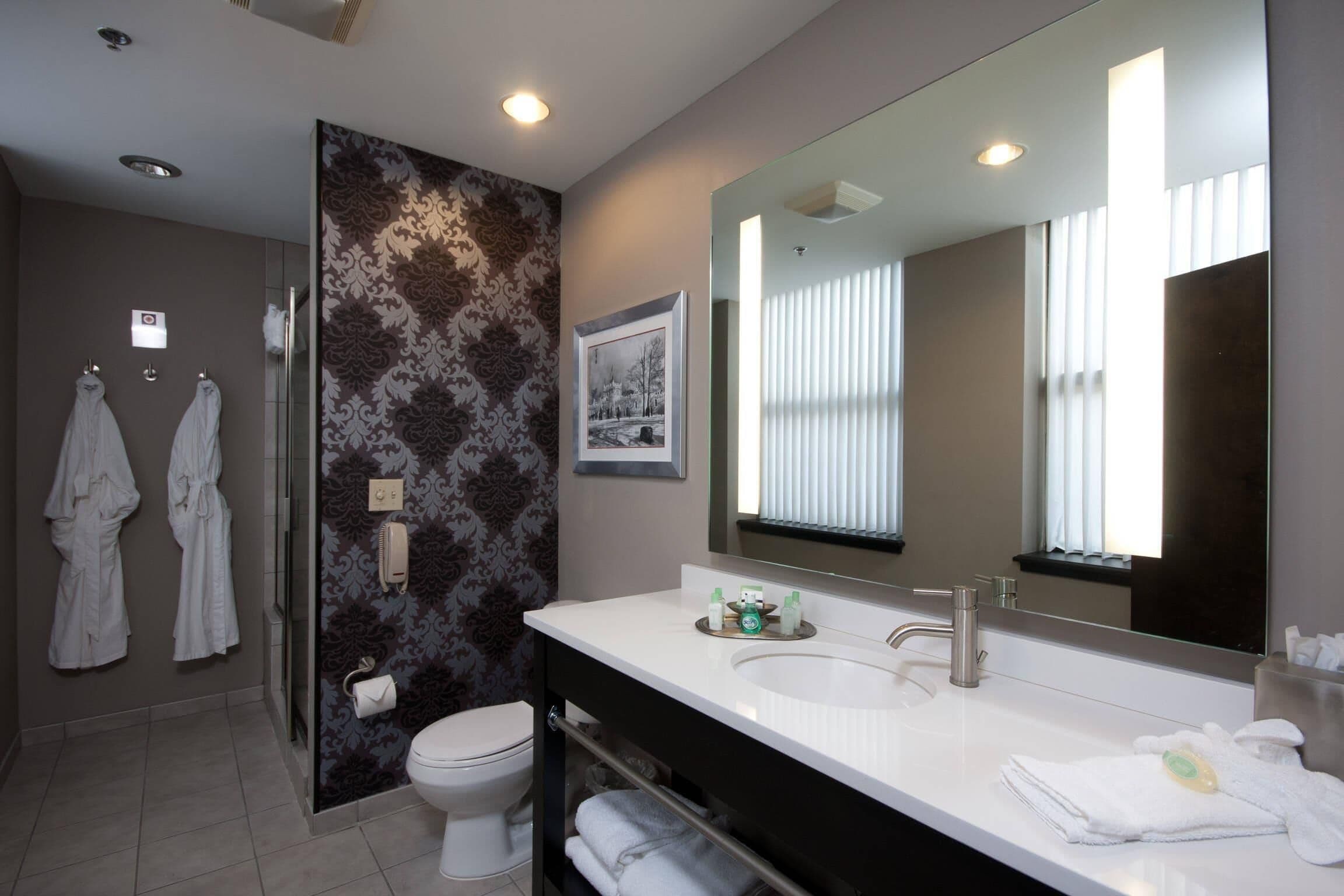Un baño moderno con un espejo grande, lavamanos blanco y dos toallas colgadas en la pared.
