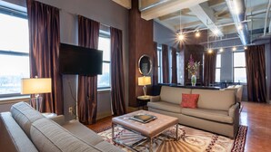 A modern living room with a sofa, ottoman, and a flat-screen TV. - The Giacomo Niagara Falls NY, an Ascend Collection Hotel (Niagara Falls)