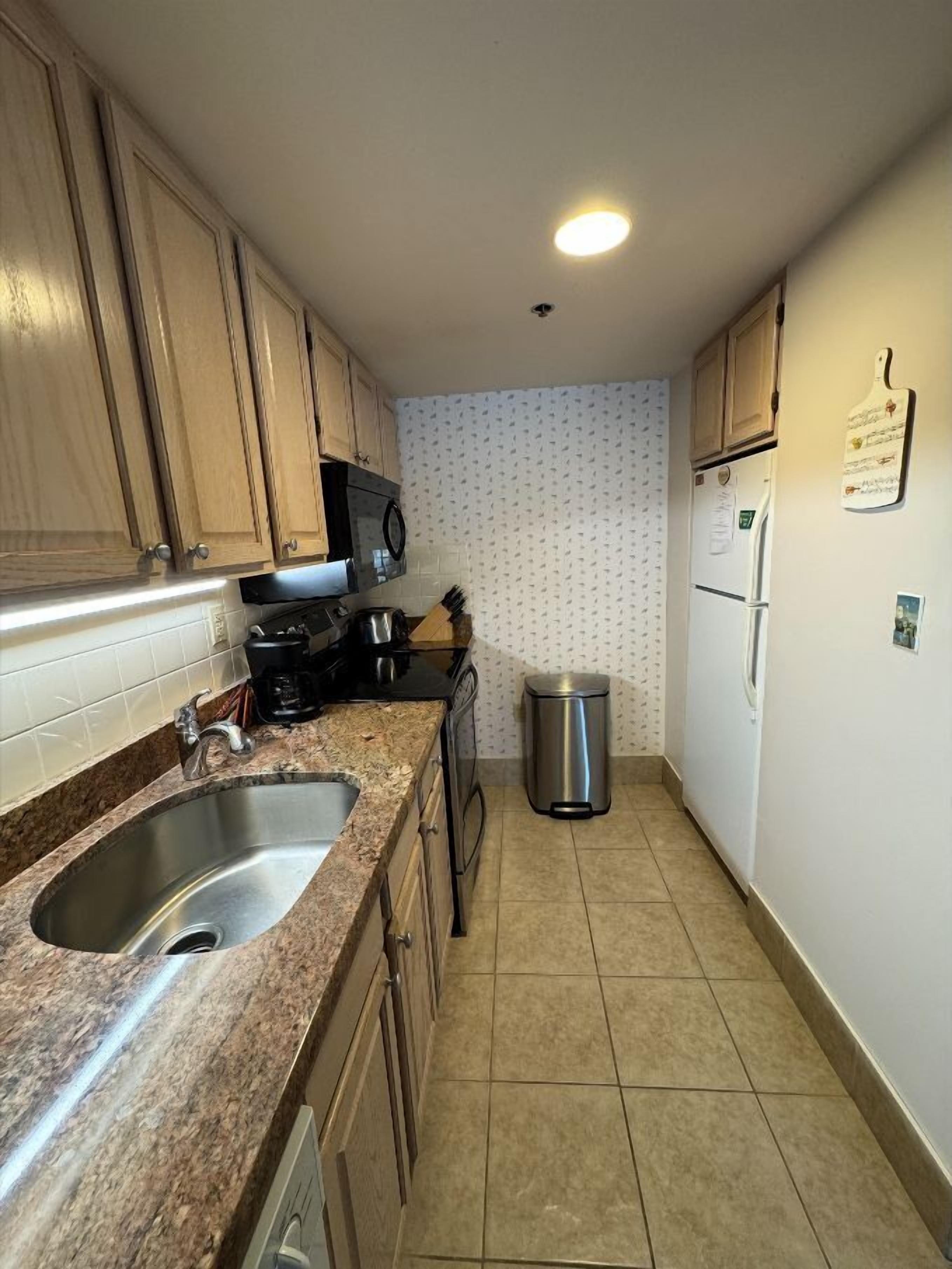 A compact kitchen with two sinks, a microwave, a refrigerator, and a trash bin.