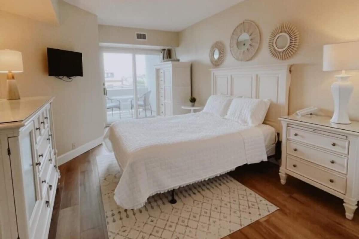 A bedroom with a bed, nightstands, a dresser, a TV, and a view of the outside.