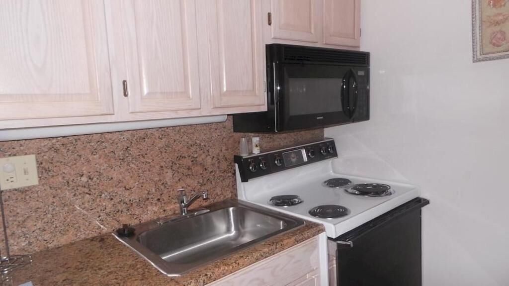 A kitchen with a granite countertop, stainless steel sink, white cabinets, a black microwave, and a white stove.