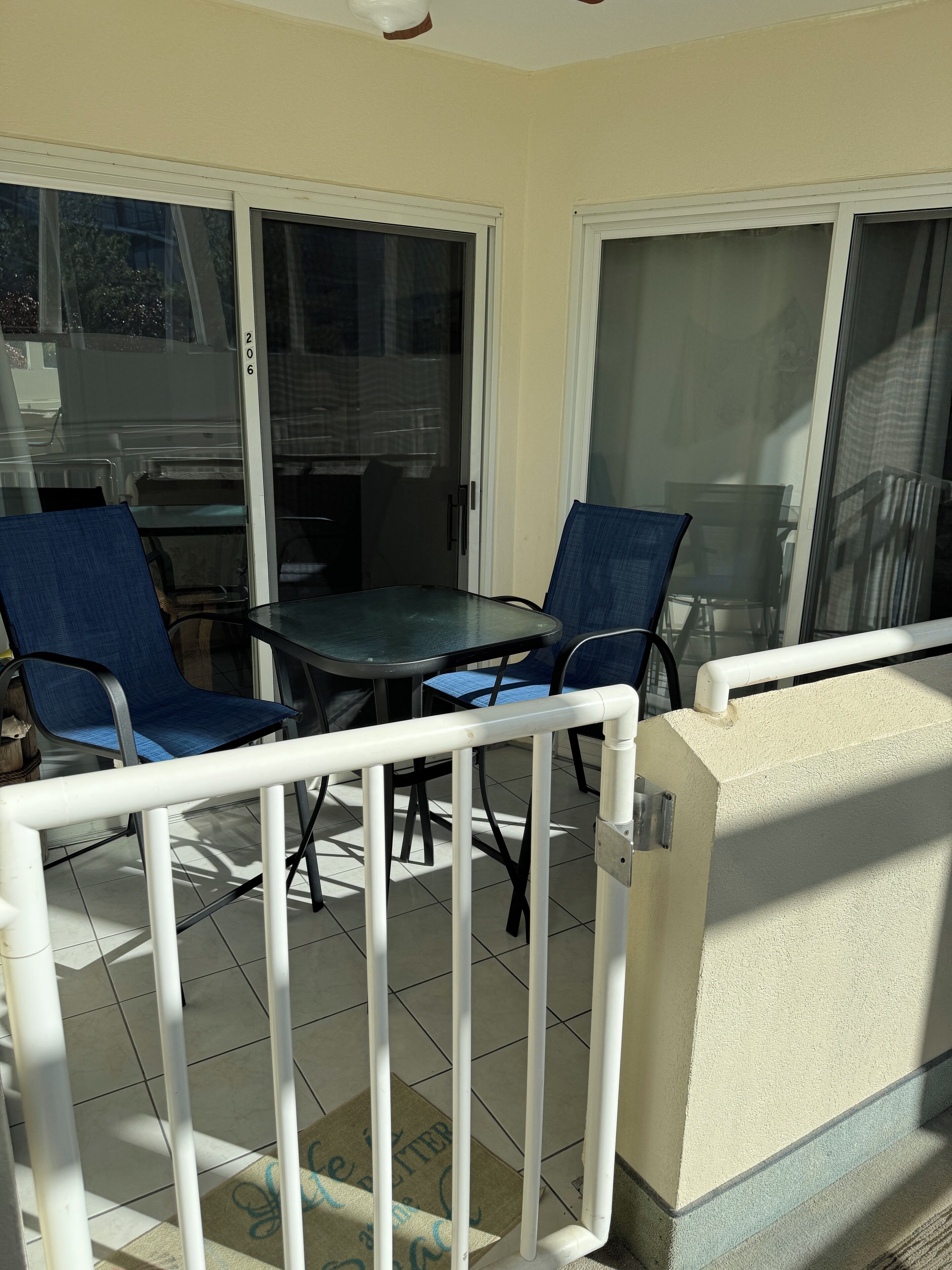 A balcony with a glass door, two chairs, a table, and a white railing.
