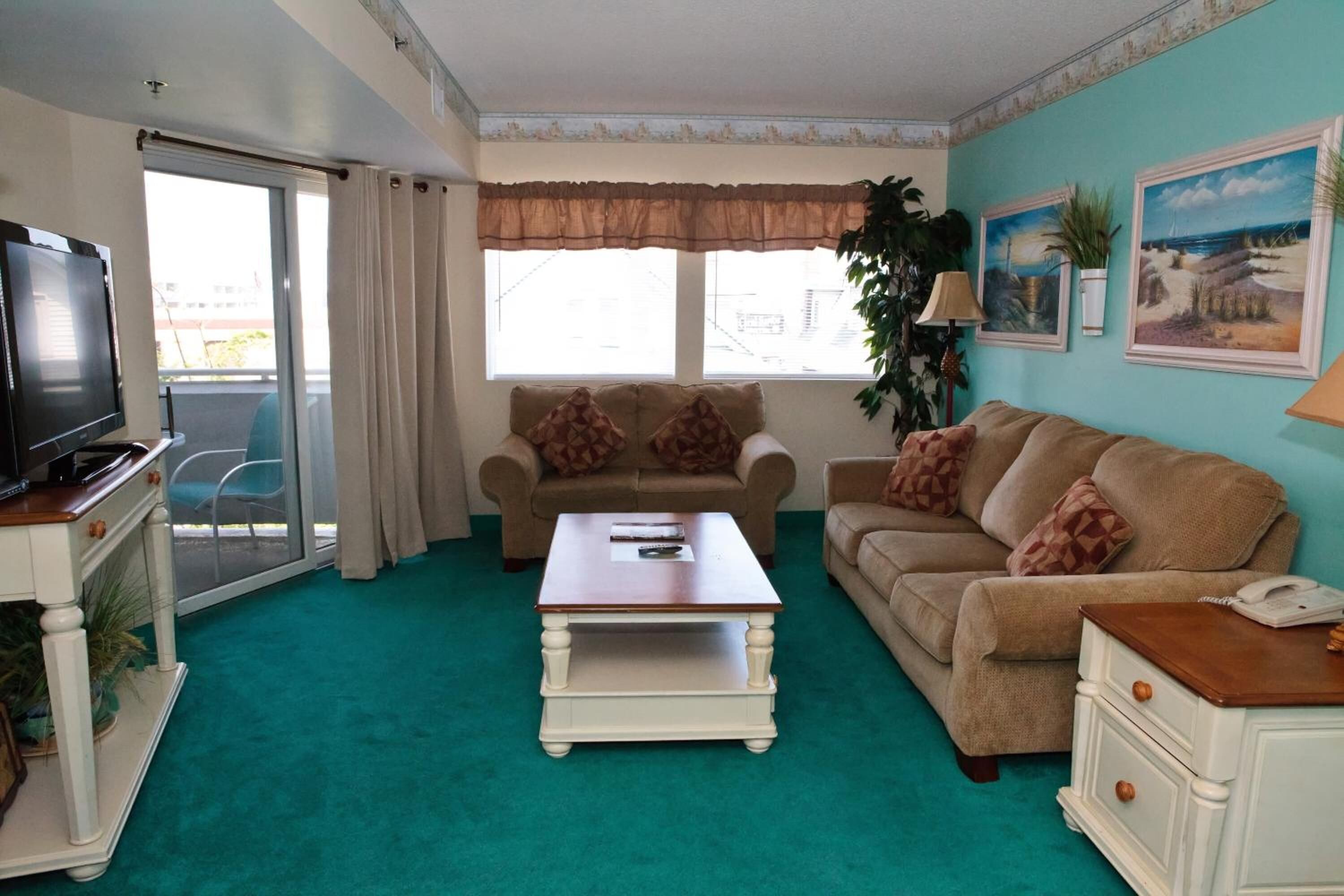 A living room with a television, two couches, a coffee table, and a sliding glass door leading to a balcony.