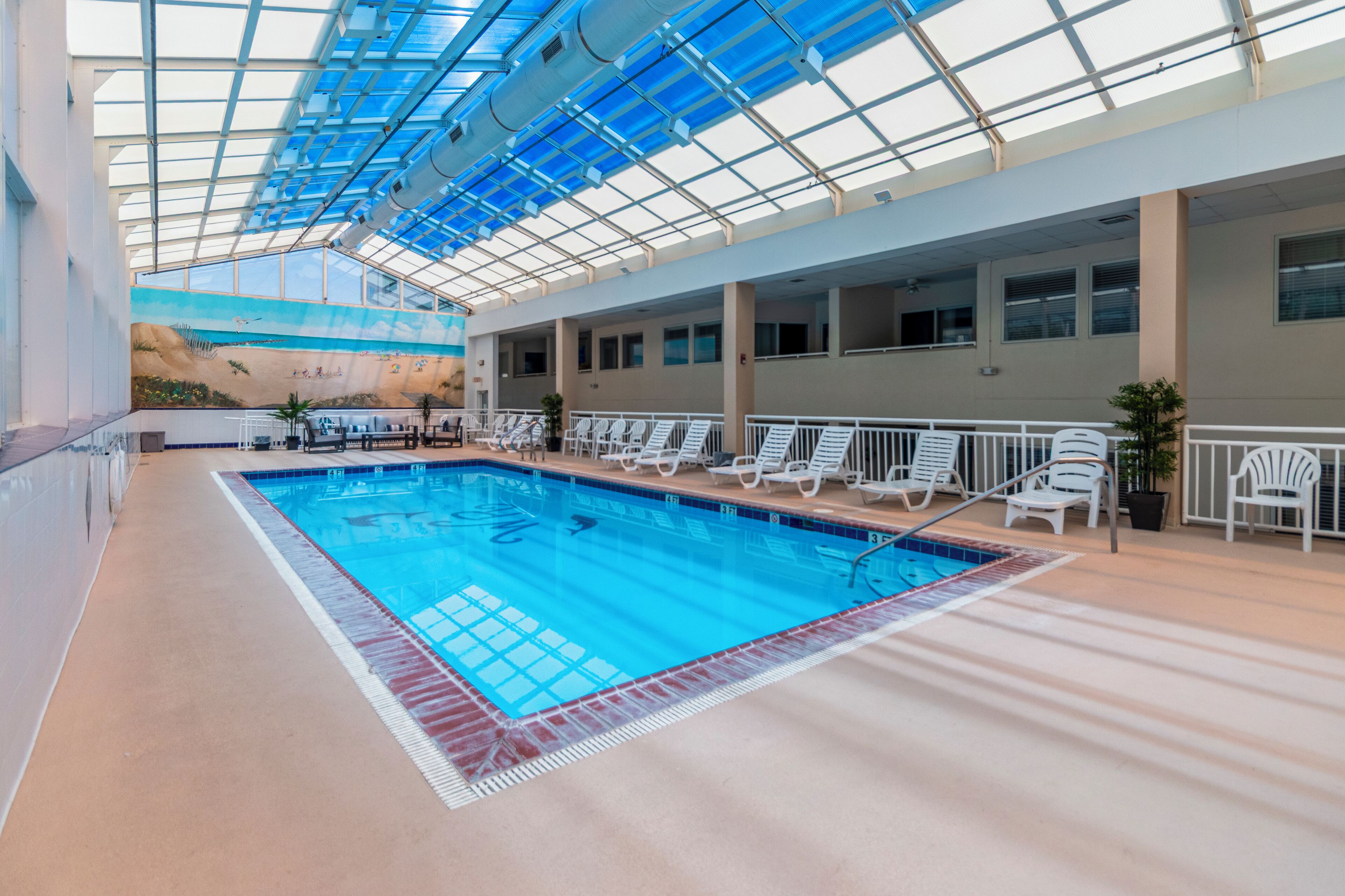 An indoor swimming pool with a glass ceiling, white lounge chairs, and a mural on the wall.