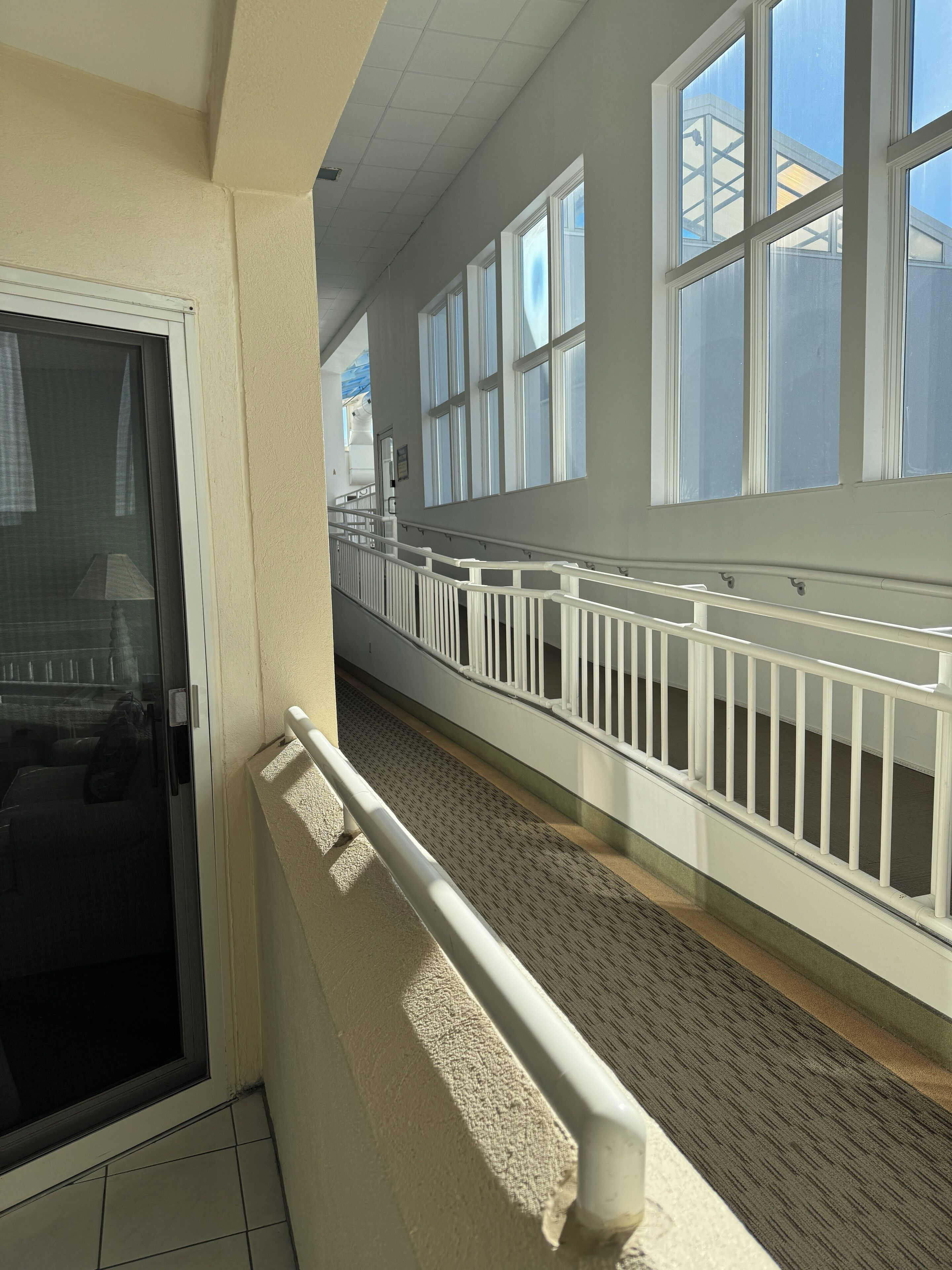 A corridor with a white railing, large windows, and a view of the sky.
