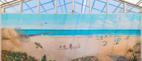 A mural of a beach scene with a staircase leading down to the water, a seagull flying, and people relaxing on the sand.