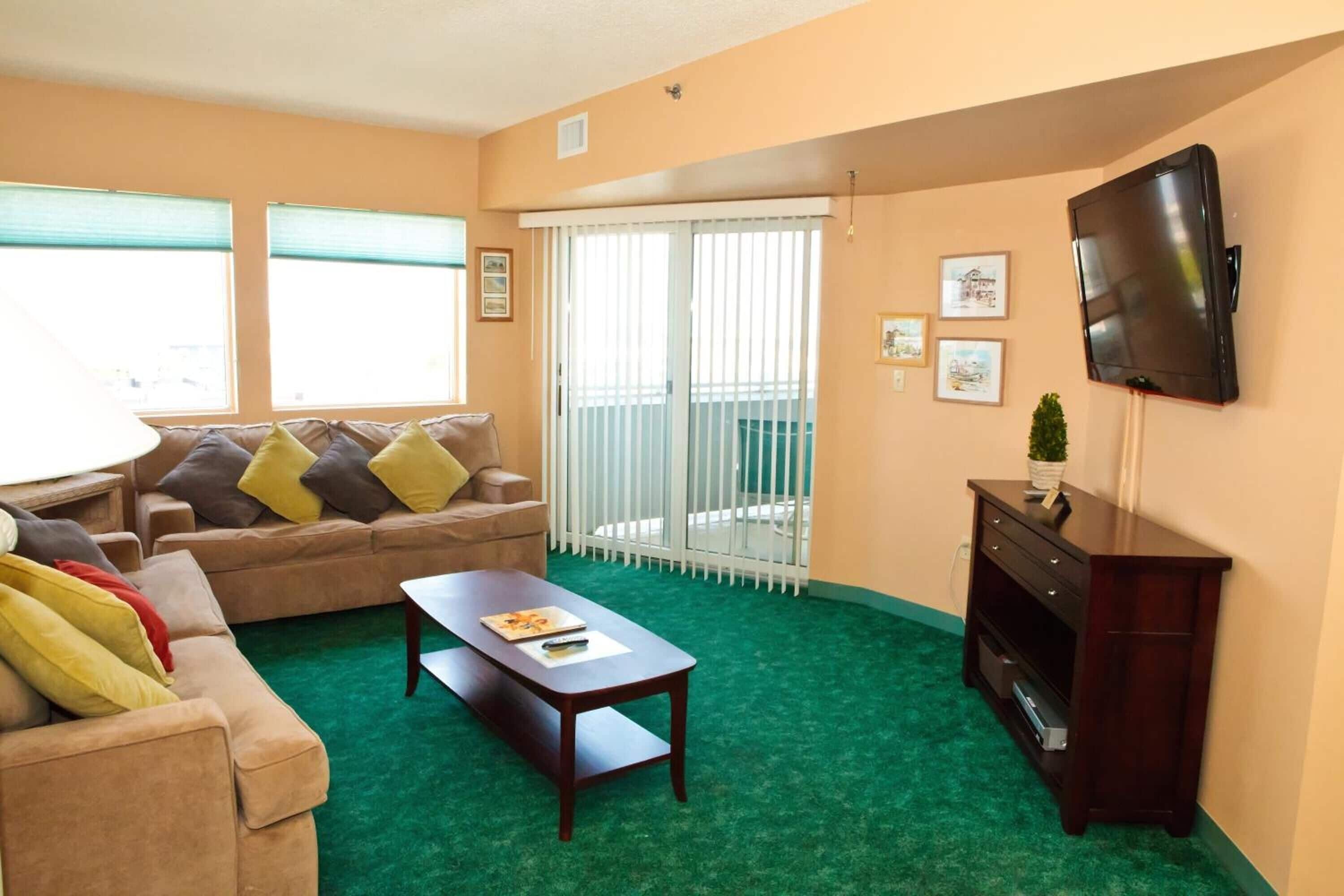 Una sala de estar con sofá, mesa de centro, televisor y balcón con puerta corrediza.
