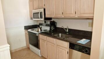 A compact kitchen with light wooden cabinets, a stainless steel sink, a microwave, a stove, and a dishwasher.