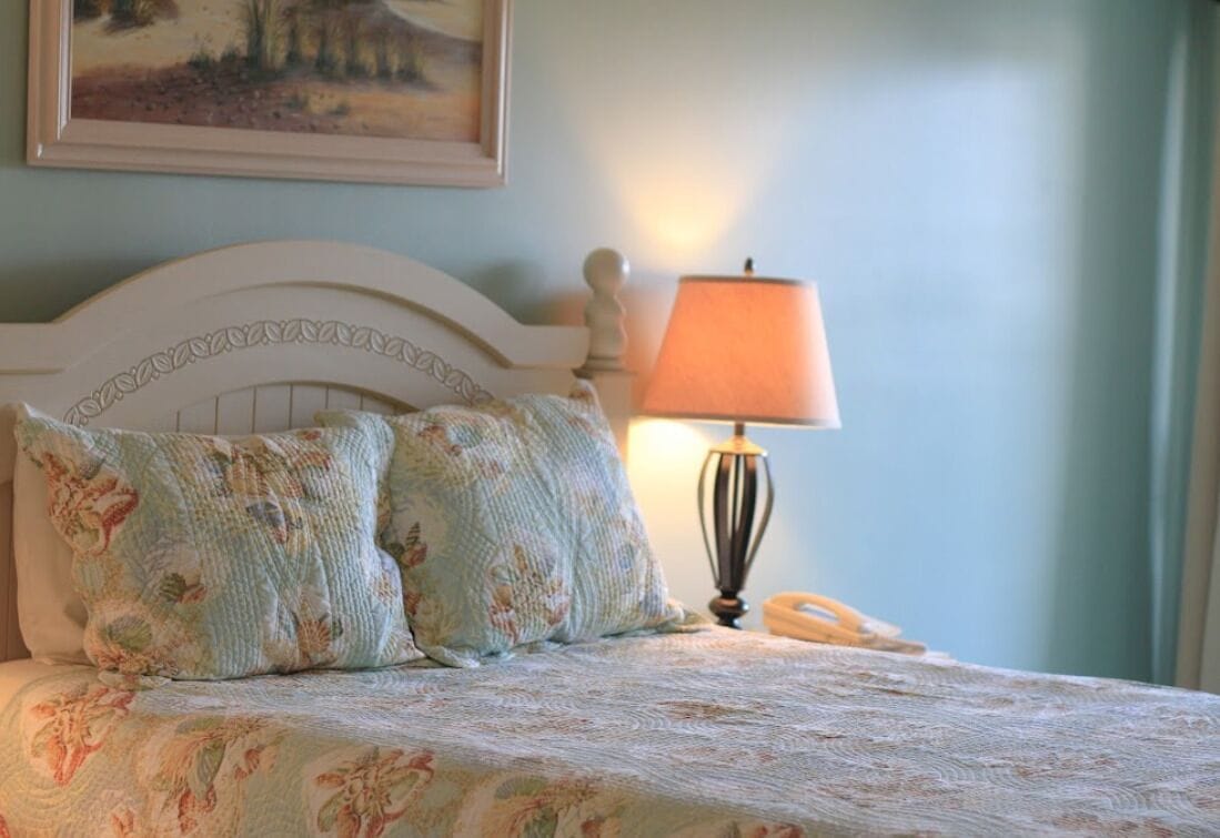 Una cama con ropa de cama de diseño floral, una lámpara de noche y un cuadro en la pared.