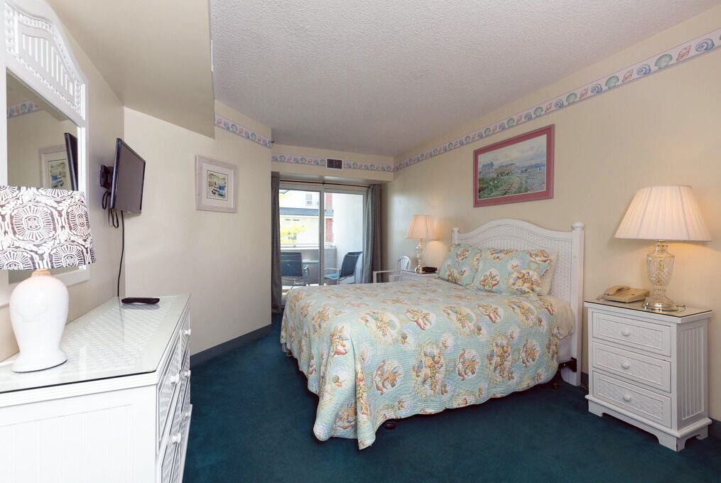 A bedroom with a bed, bedside tables, a dresser, a TV, and a window.