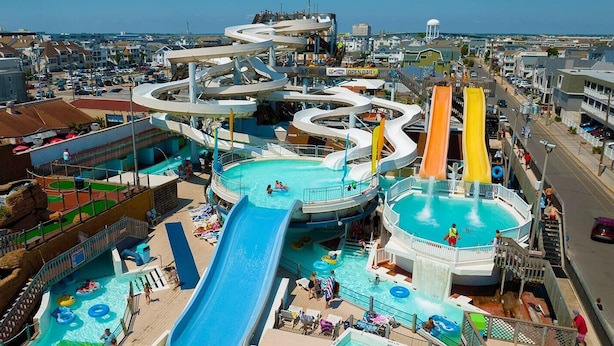 Parque acuático con múltiples toboganes y piscinas, rodeado de edificios y un cielo despejado.