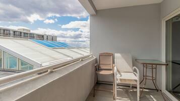 Een balkon met een stoel, een tafeltje en uitzicht op de lucht en wolken.