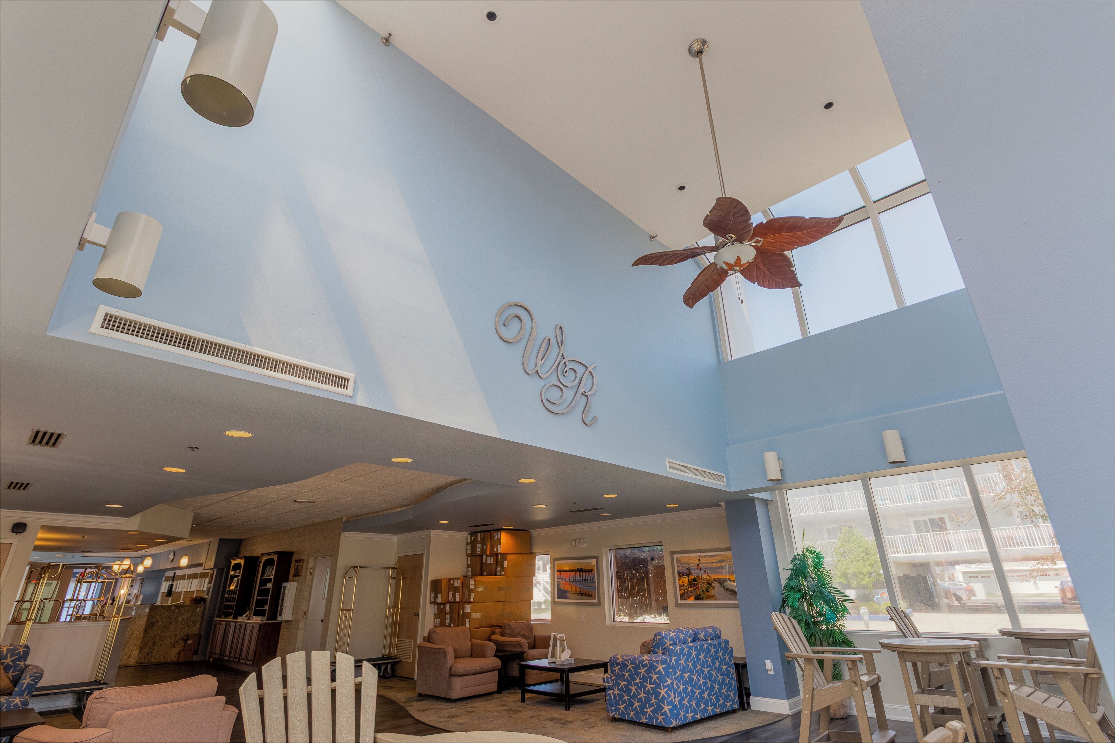 A spacious lobby with a high ceiling, ceiling fans, and large windows offering views of the outside.