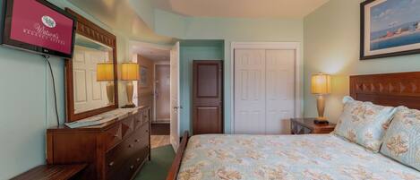 A bedroom with a bed, dresser, TV, and a door leading to another room.