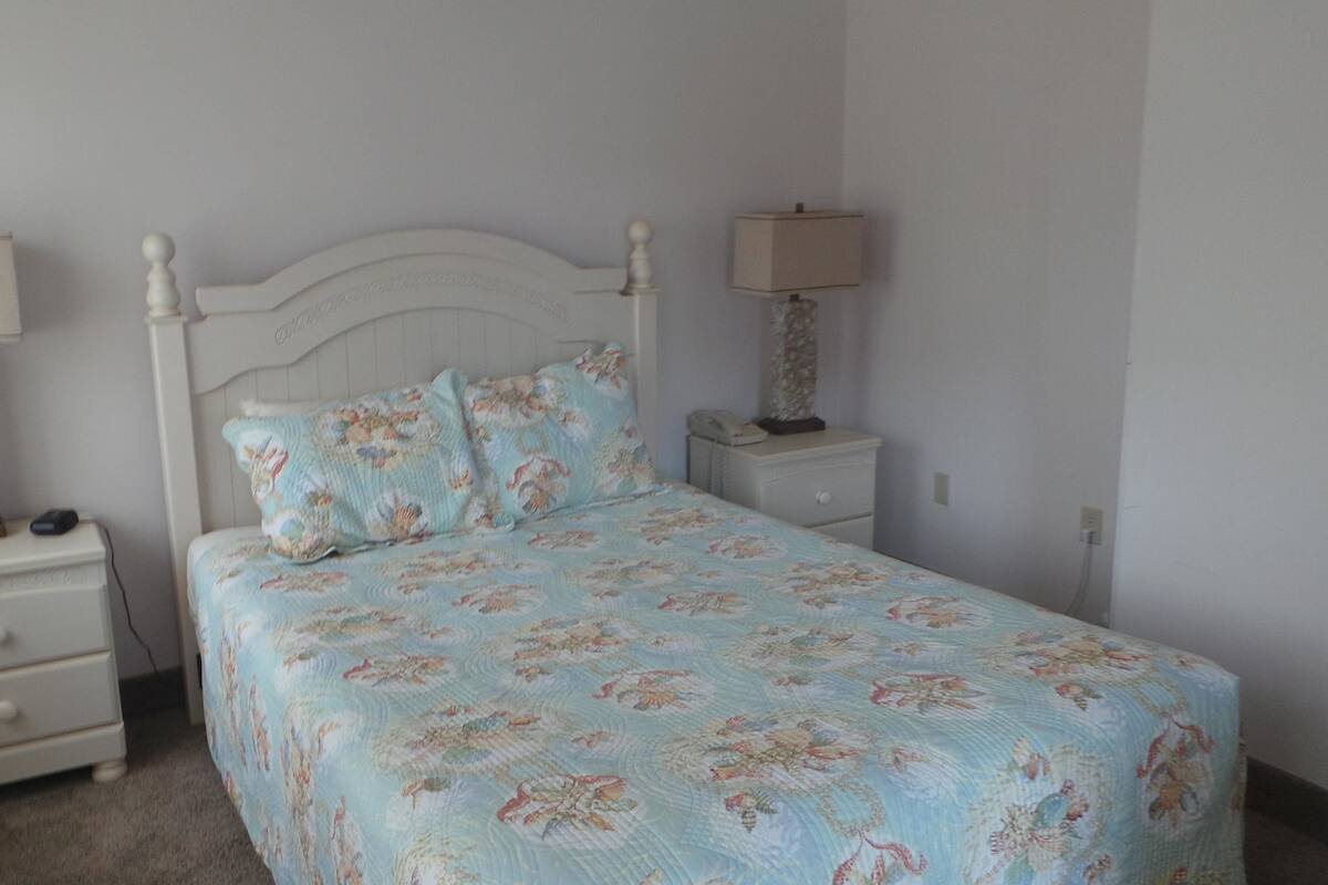 A bedroom with a bed, two bedside tables, a nightstand, a lamp, and a dresser.
