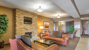 Un vestíbulo de hotel con sofás de cuero, pared de piedra, televisor de pantalla plana, chimenea y un pasillo que conduce a un ascensor.