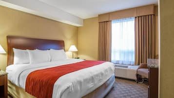 Une chambre d’hôtel avec un grand lit, deux tables de chevet, un bureau, une chaise et une fenêtre avec des rideaux.