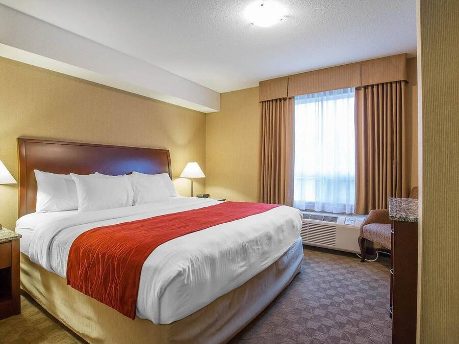 Une chambre d’hôtel avec un grand lit, deux tables de chevet, un bureau, une chaise et une fenêtre avec des rideaux.