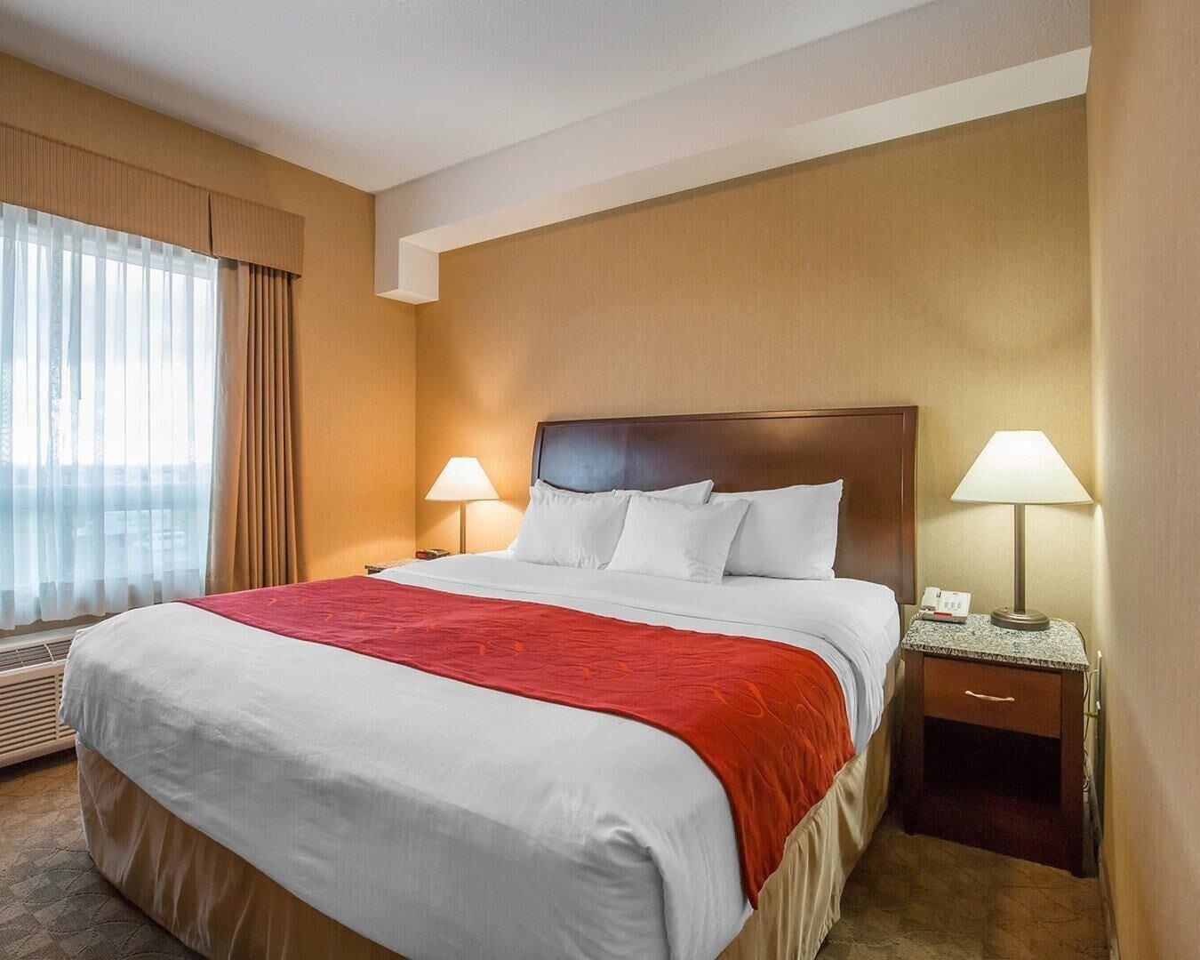 A hotel room with a large bed, two bedside lamps, a nightstand, and a window with curtains.