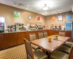 A hotel breakfast area with a buffet, coffee machines, and a clock on the wall.
