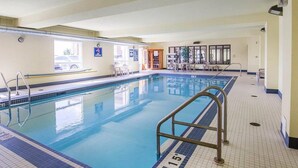 Una piscina interior con carriles delimitados, una silla de salvavidas y una zona de estar con mesas y sillas.
