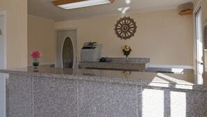 A reception area with a granite counter, a printer, a decorative wall piece, and a door with a glass panel. - Sunrise Inn (Jasper)