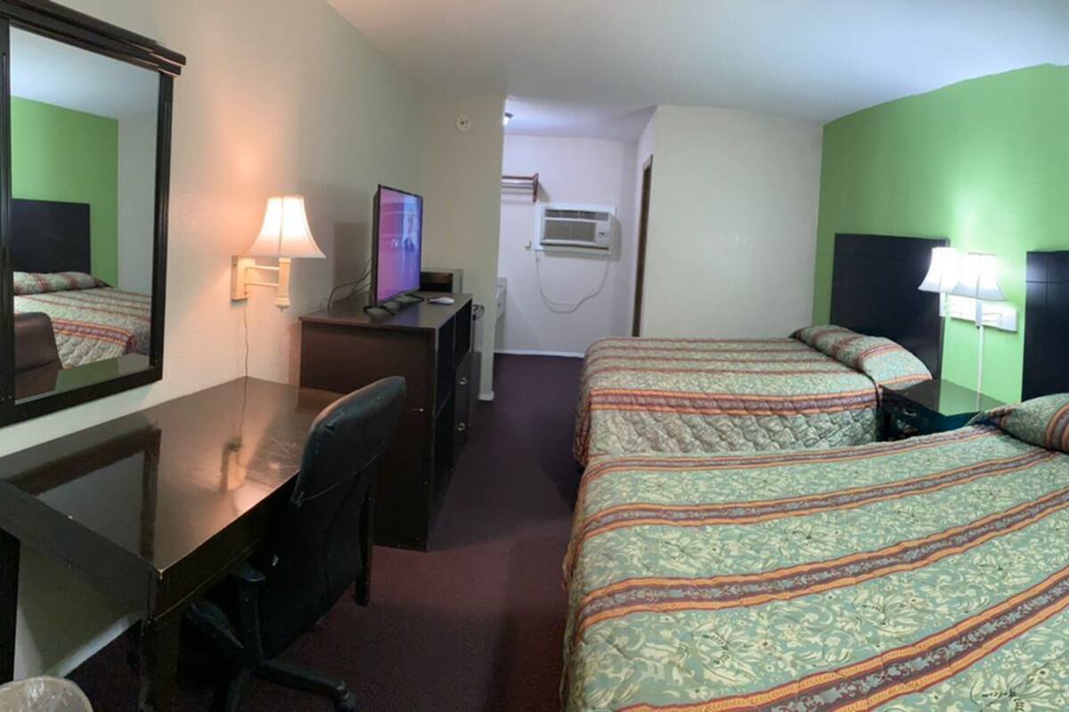 A hotel room with two beds, a desk with a computer, a mirror, and a window with curtains.