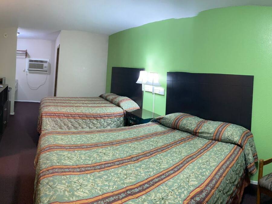 A hotel room with two beds, a desk with a computer, a mirror, and a window with curtains.