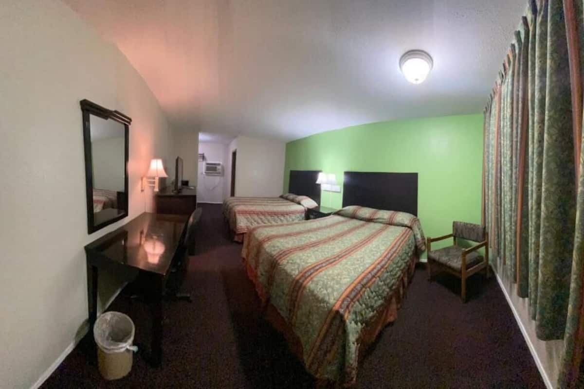 A hotel room with two beds, a desk, a chair, a mirror, and a window with curtains.