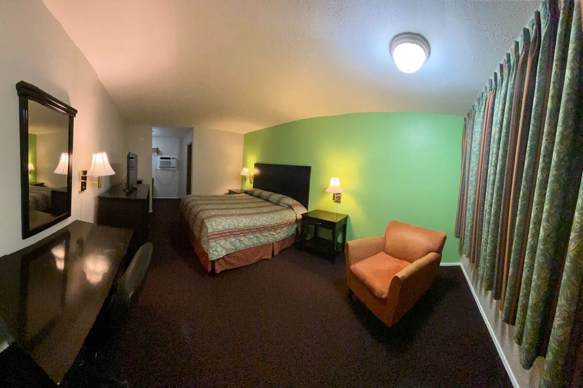 A hotel room with a bed, a chair, a desk, a mirror, and a green accent wall.