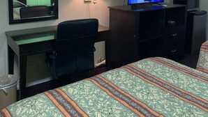 A hotel room with a bed, a desk with a chair, a television, a mirror, and a lamp. - Sunrise Inn (Jasper)